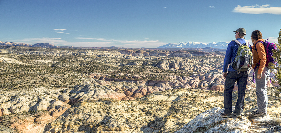 A man and a woman stand on cliff looking out over the Grand Staircase- Escalante