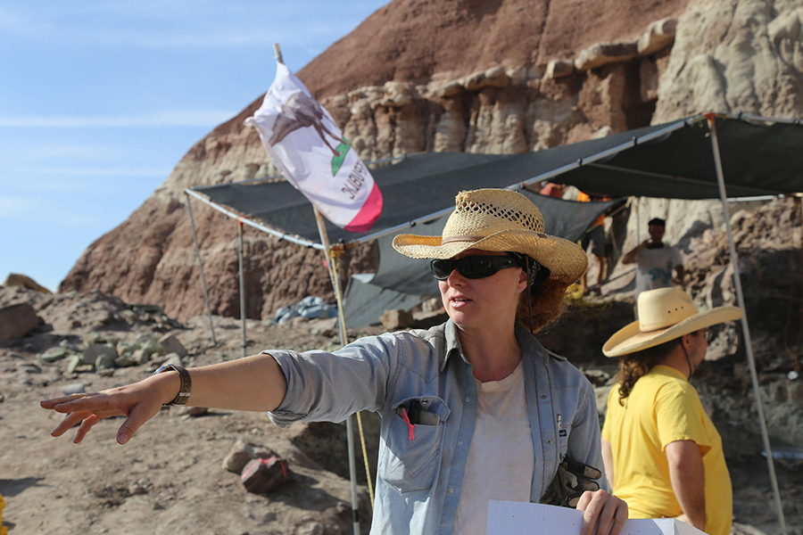Dr. Alyssa Bell points to where the bone that led to the quarry was discovered. The quarry is the tented area in the background, where researchers dig into the side of a hill to find more bones. CREDIT KATE GROETZINGER / KUER